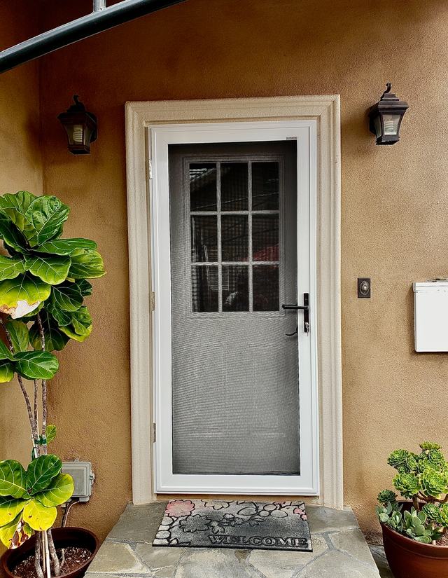 White hinged security screen door over a front door with a nine-pane window, between two porch lanterns
