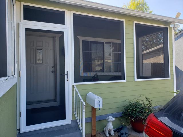 Front porch of a green home enclosed with a white-framed hinged security screen door and fixed security screen panels