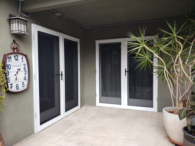 Two pairs of white French-door security screens meeting at the corner of a covered patio