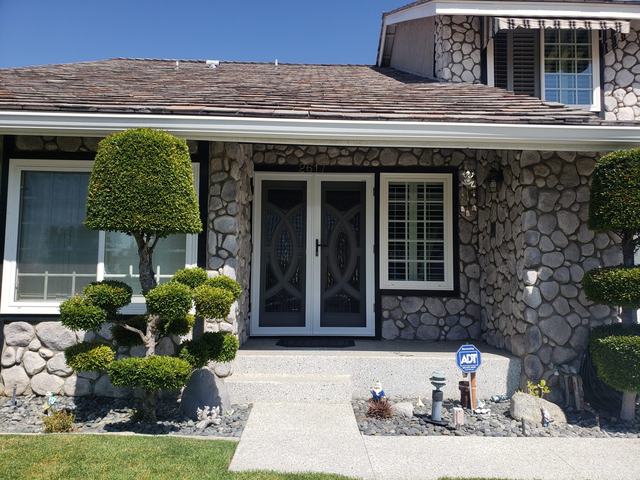 White double security screen doors on the front entry of a stone-clad home with clipped shrubs