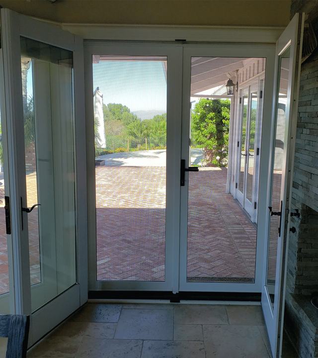 View from inside through white French-door security screens onto a brick patio