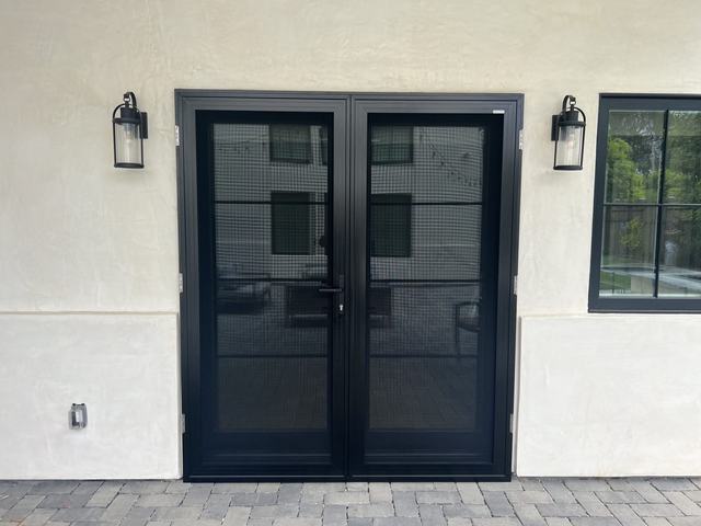 Black double security screen doors between two lanterns on a white stucco wall