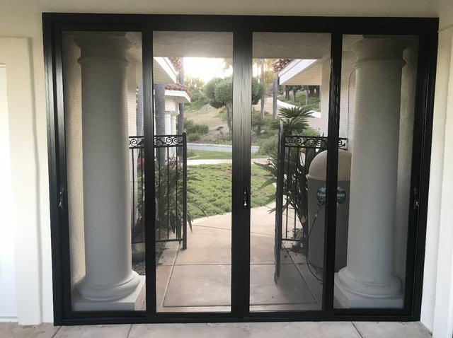 Black four-panel sliding security screen door looking out to porch columns and a garden path