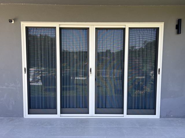 White four-panel sliding security screen door on a gray stucco wall