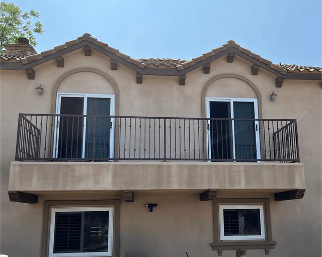 Two white sliding security screen doors on an upstairs balcony of a Spanish-style home