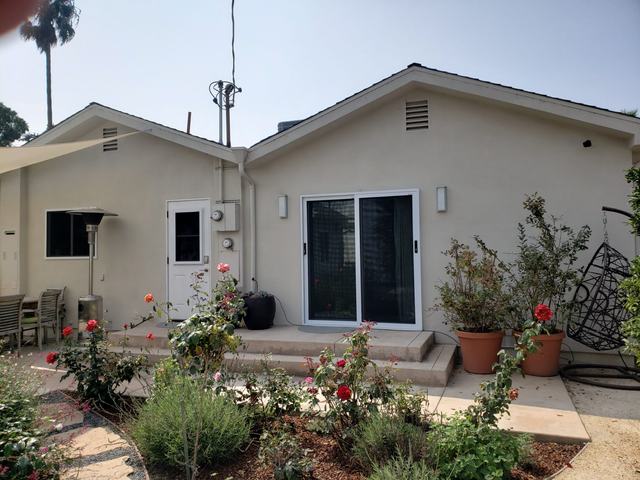 White sliding security screen door at the back of a single-story home with a rose garden
