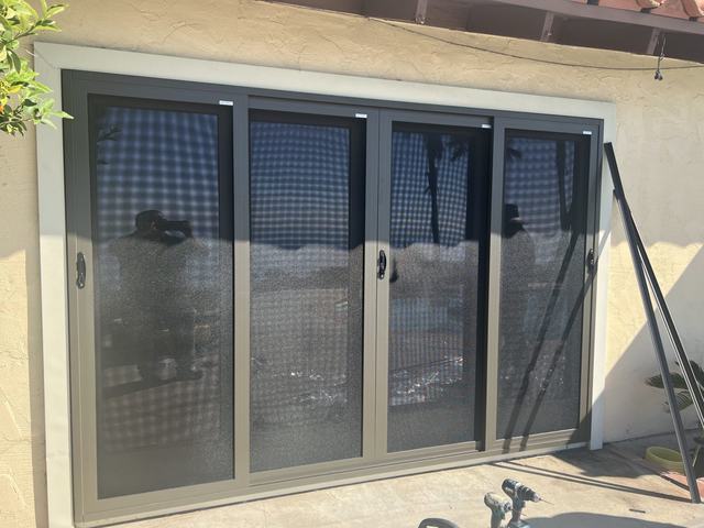 Bronze four-panel sliding security screen door on a stucco patio wall