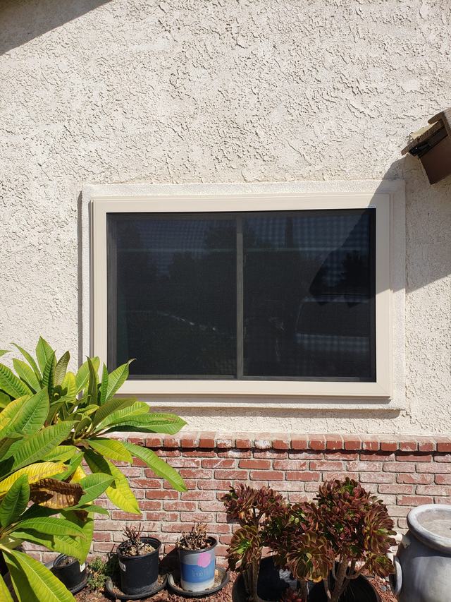 Beige-framed fire-escape security screen on a sliding window in a stucco and brick wall