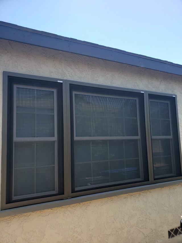 Bronze fixed security screens covering a three-part window on a stucco home