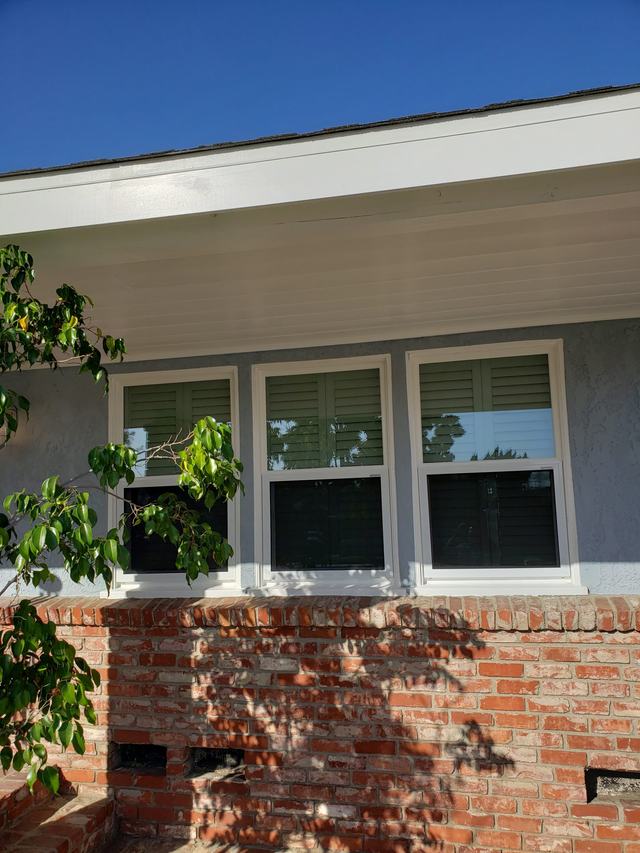 Three white-framed fixed security screens on windows above a brick planter