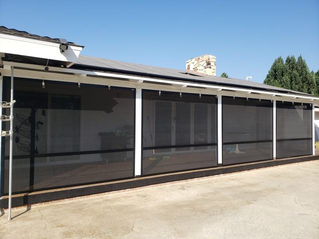 Long covered patio enclosed with security screen panels between white posts